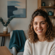 A diverse woman in her late 20s smiling genuinely, looking at the camera. Soft-focus background with subtle teal and blue ton